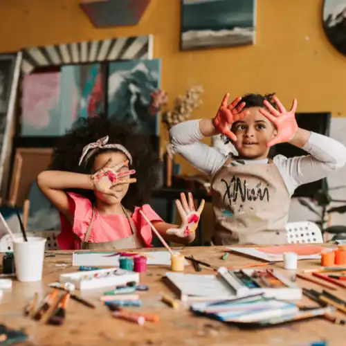 Two young kids happily painting and building fine motor skills at a craft table.