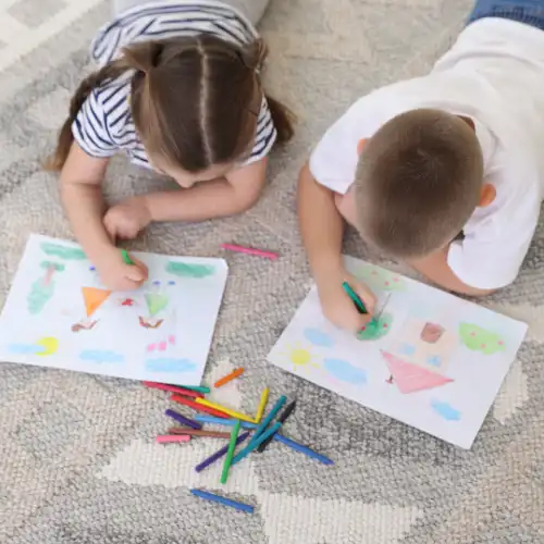 Brother and sister lying on the floor focused on coloring their printable worksheets.